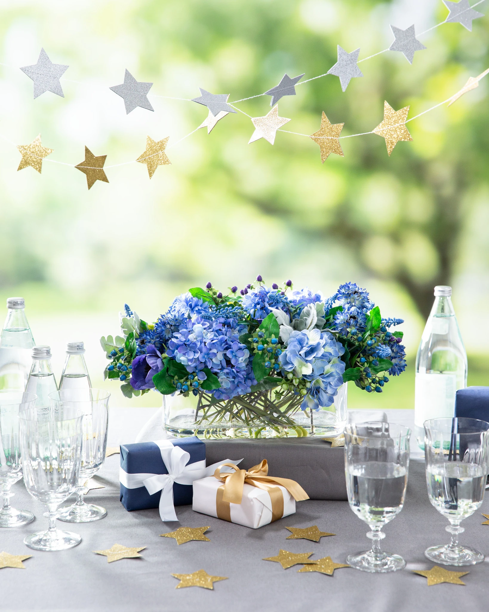 Blue floral centerpiece on a table with drinking glasses, a star garland, and wrapped presents